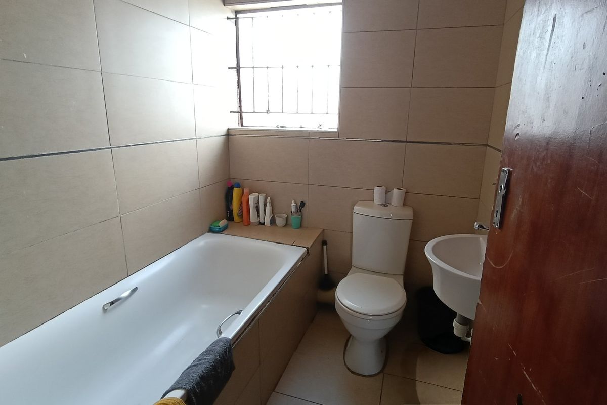 A functional bathroom featuring a built-in bathtub, pedestal basin, and toilet, finished with neutral ceramic wall and floor tiles.