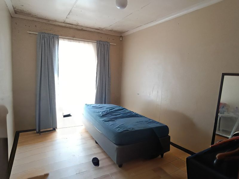 A bedroom featuring timber flooring and a sliding door, currently showing significant signs of ceiling water damage and wall surface deterioration.