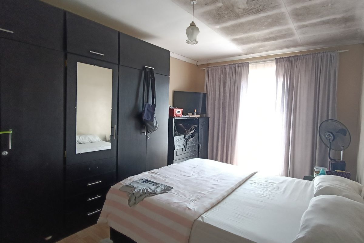 A bedroom featuring built-in cupboards, with visible water damage and staining on the ceiling requiring maintenance.