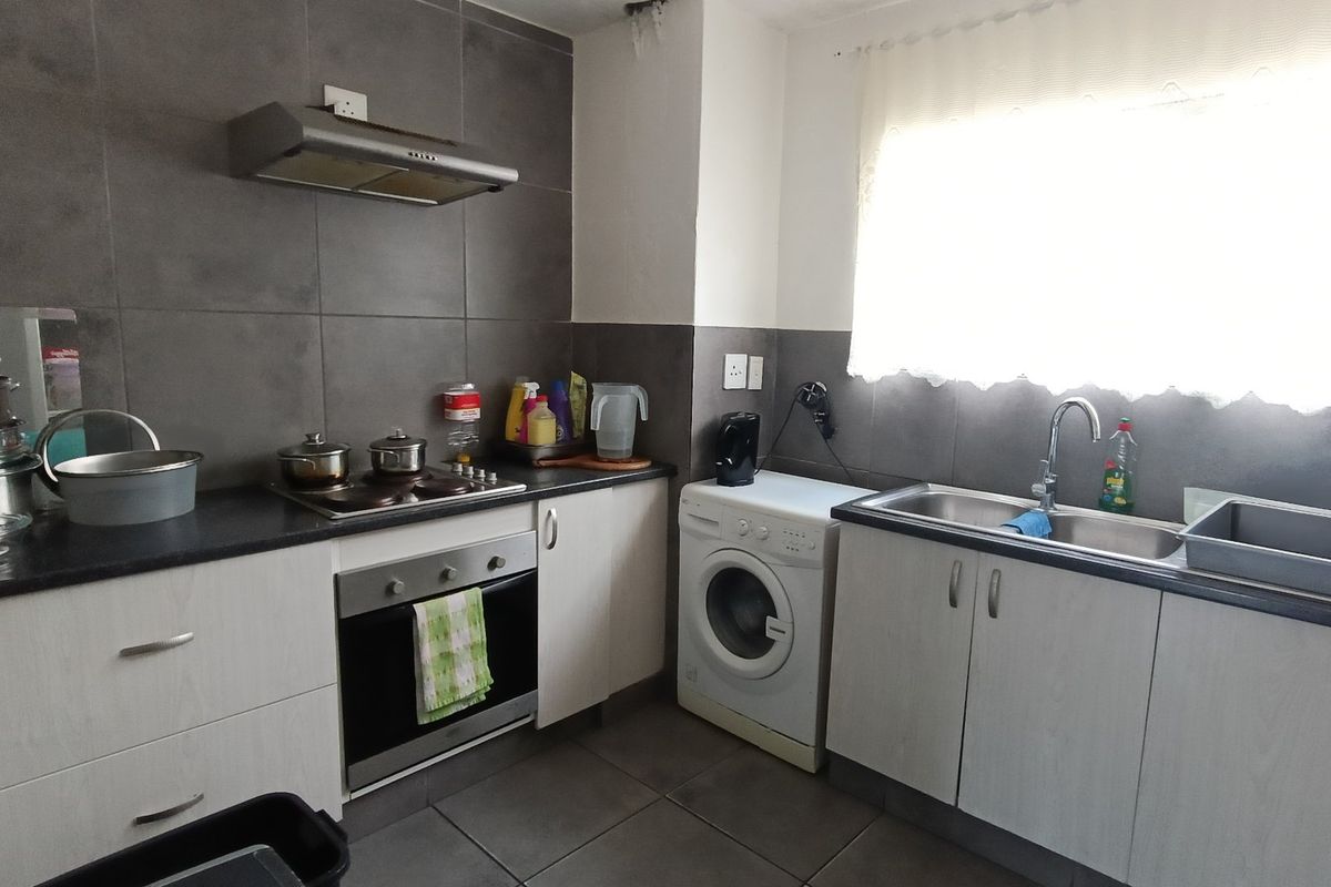 A functional kitchen featuring built-in cabinetry, a stainless steel sink, electric hob, oven, and extractor fan with modern grey tiled splashbacks.
