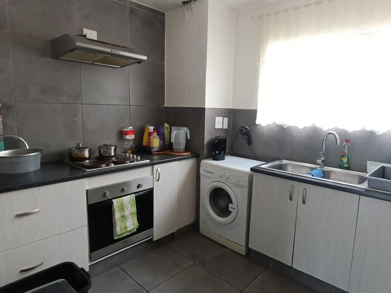 A functional kitchen featuring built-in cabinetry, a stainless steel sink, electric hob, oven, and extractor fan with modern grey tiled splashbacks.