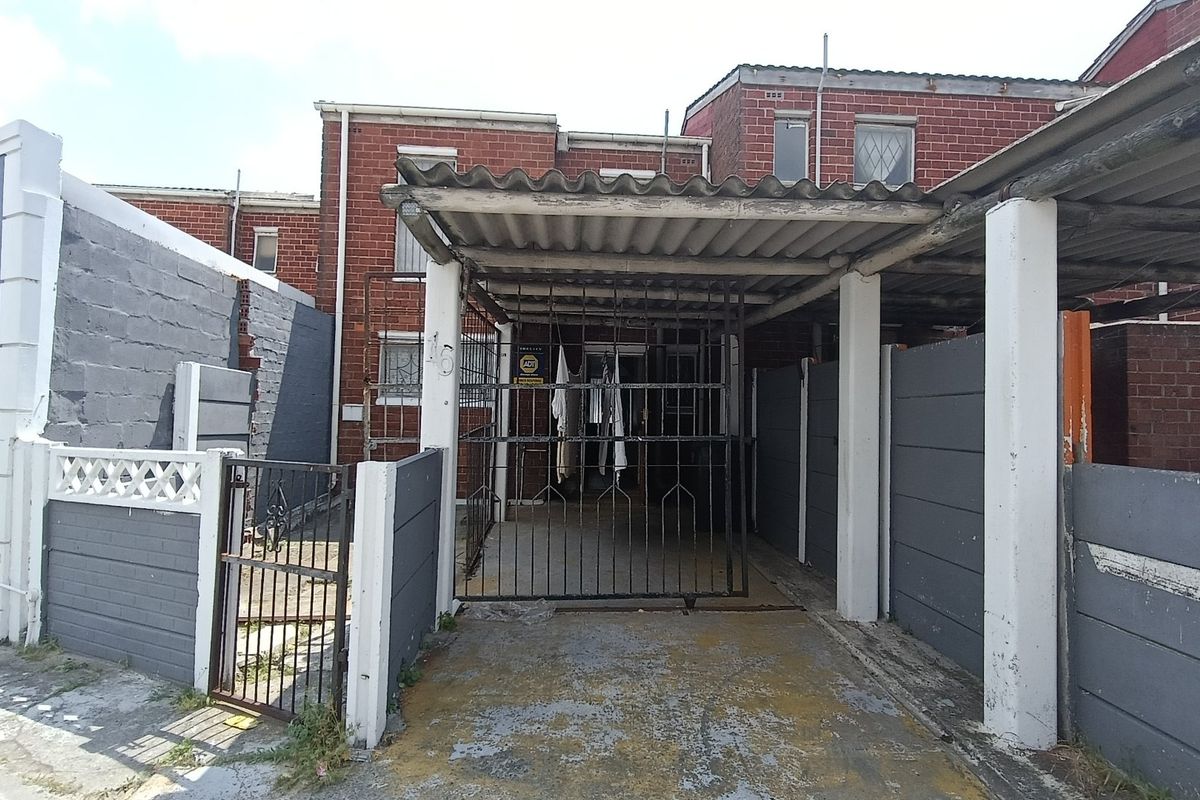 Front exterior view of the property featuring a covered carport, security gate, and brick facade with boundary walling.