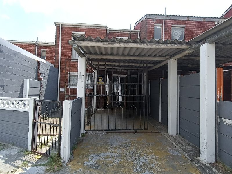 Front exterior view of the property featuring a covered carport, security gate, and brick facade with boundary walling.