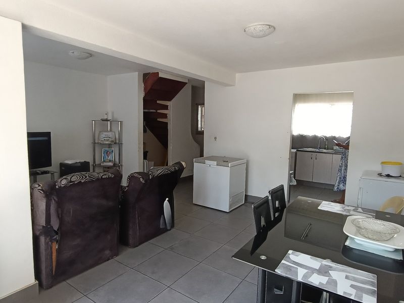 Open plan living and dining area featuring tiled flooring, leading to a functional kitchen space and an internal staircase.