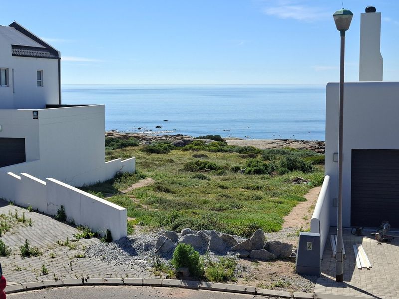 Vacant residential plot situated between existing properties, featuring direct coastal views and paved driveway access.