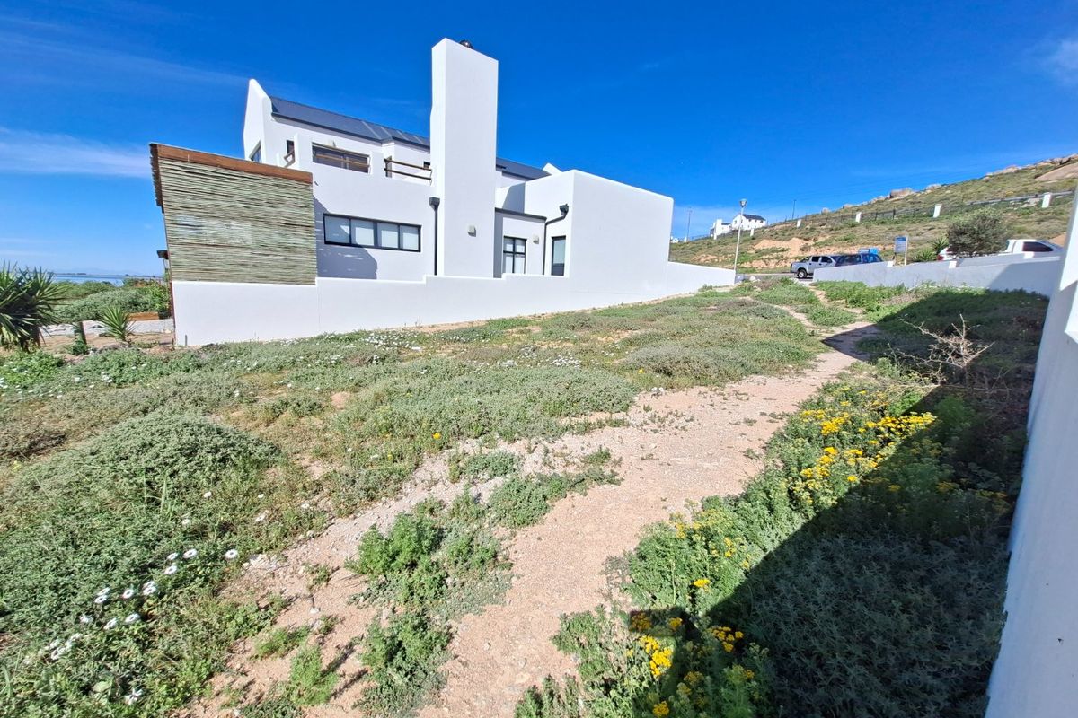 Rear view of a modern white residential property featuring a prominent chimney, boundary wall, and natural landscaping.