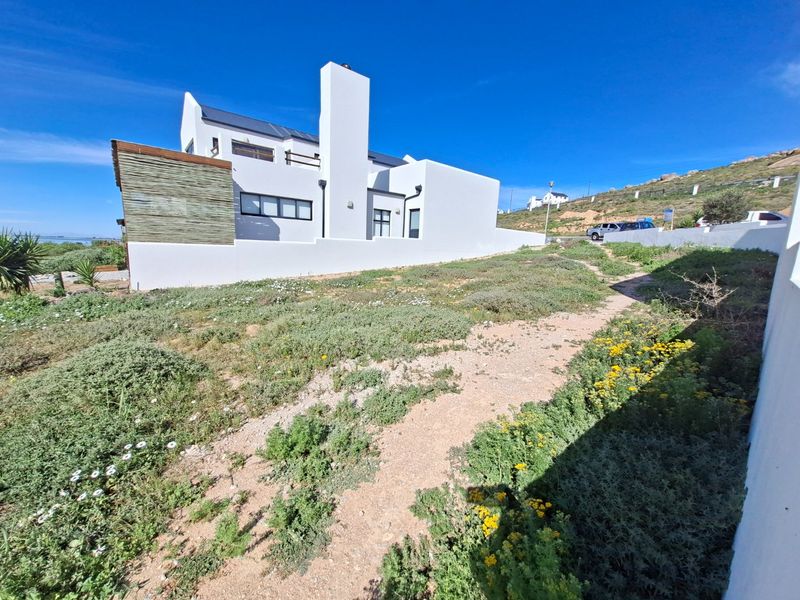 Rear view of a modern white residential property featuring a prominent chimney, boundary wall, and natural landscaping.