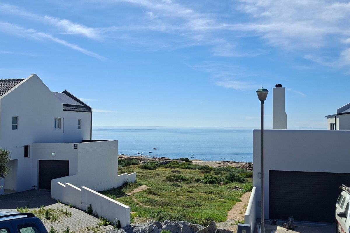 A scenic view of the ocean and coastal landscape from between two modern residential properties with paved driveways.