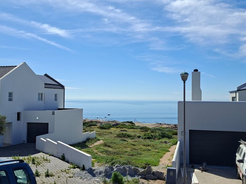 A scenic view of the ocean and coastal landscape from between two modern residential properties with paved driveways.