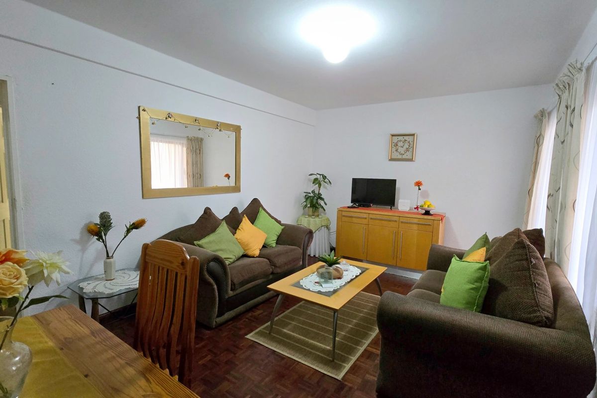 A comfortable living room featuring classic parquet flooring and access to a balcony through a sliding glass door, offering a bright and functional space.