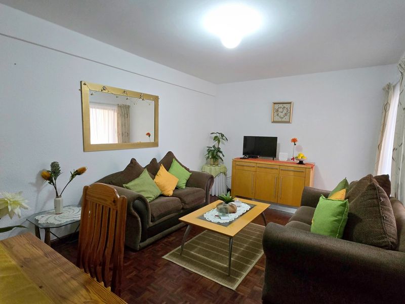 A comfortable living room featuring classic parquet flooring and access to a balcony through a sliding glass door, offering a bright and functional space.
