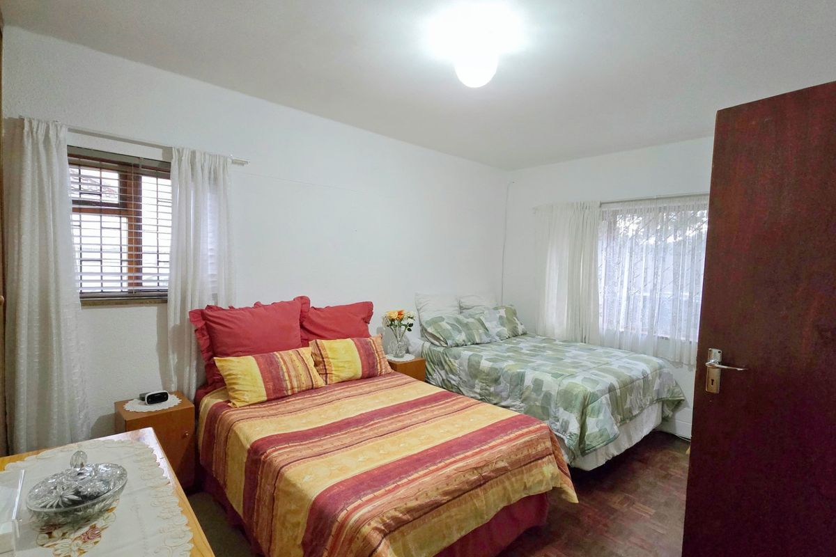 A functional bedroom featuring parquet flooring, built-in cupboards, and dual window access with fitted blinds.