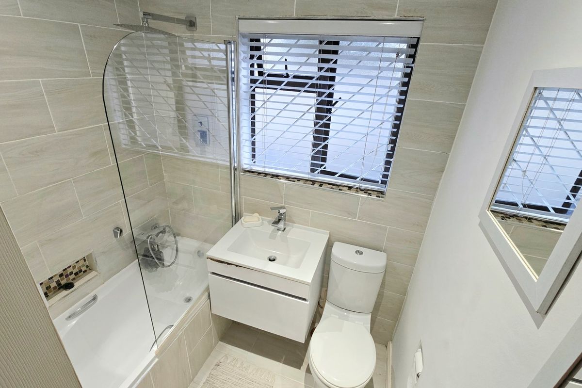 Modern bathroom featuring a bathtub with a glass shower screen, wall-mounted vanity, and neutral tiled walls.