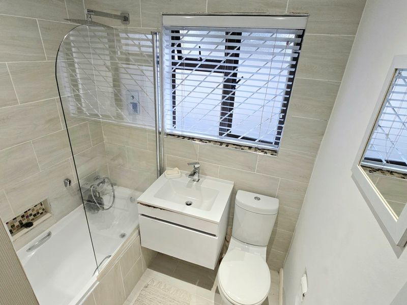 Modern bathroom featuring a bathtub with a glass shower screen, wall-mounted vanity, and neutral tiled walls.
