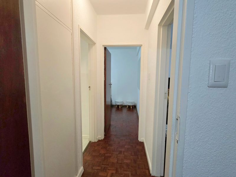 A clean, functional hallway featuring classic parquet flooring and built-in storage, providing access to multiple rooms within the apartment.