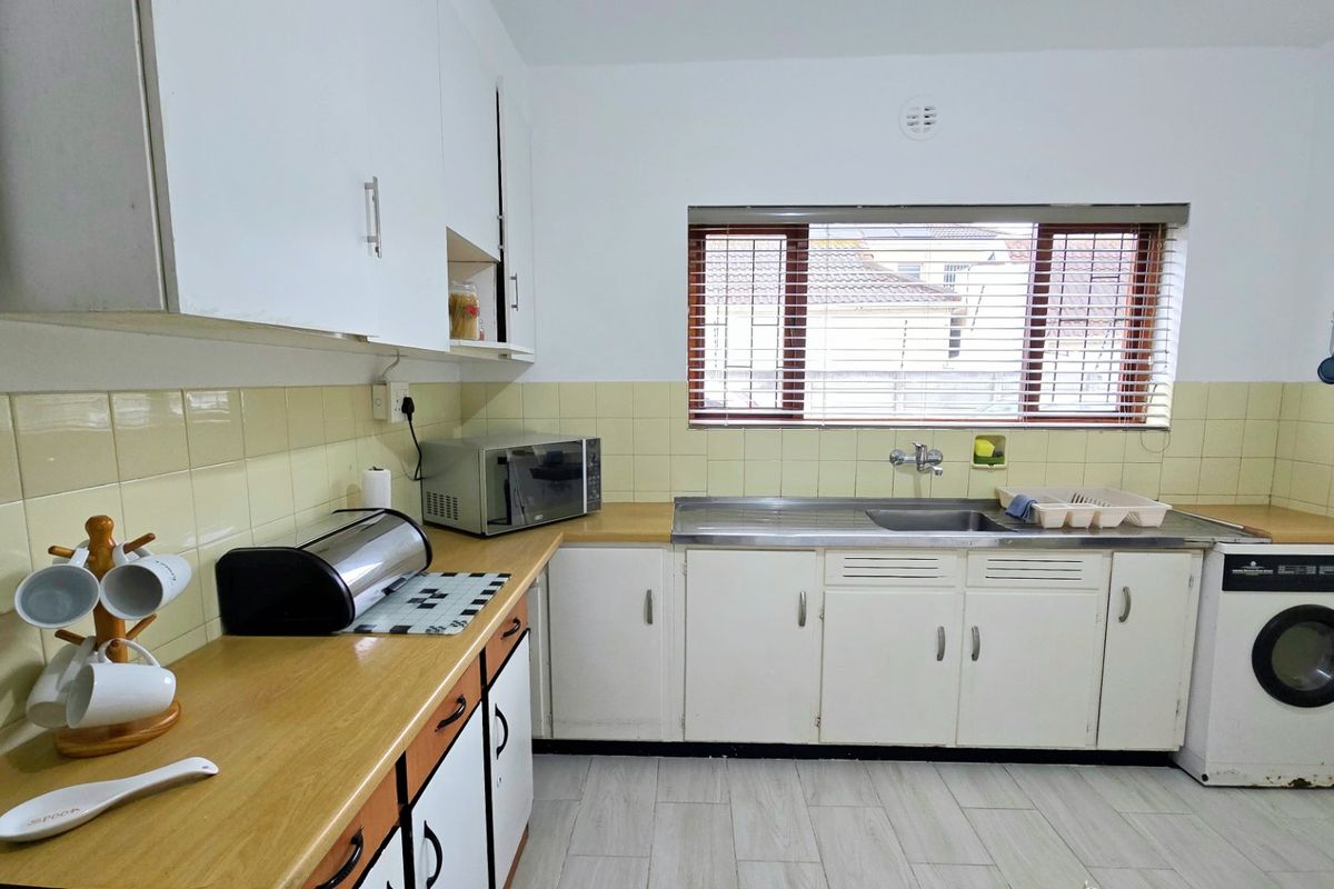 Functional kitchen featuring white cabinetry, laminate countertops, tiled backsplash, and a dedicated space for a washing machine under the counter.