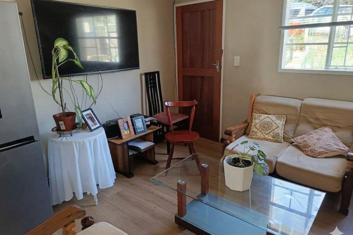 A compact living room featuring laminate flooring, a timber door, and a window with blinds, providing a functional and cozy living space.
