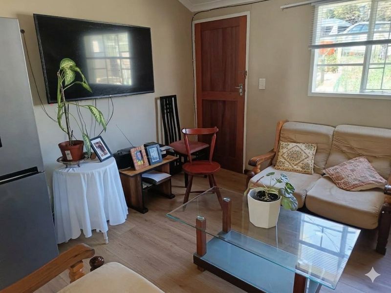 A compact living room featuring laminate flooring, a timber door, and a window with blinds, providing a functional and cozy living space.