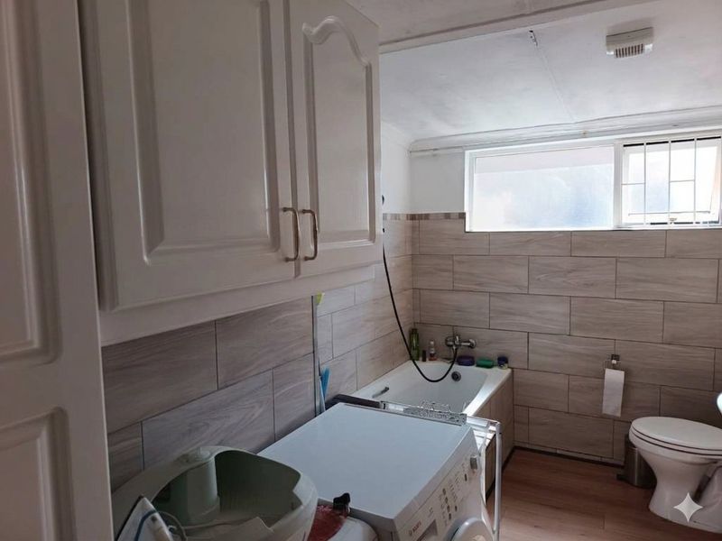 A functional laundry area featuring built-in cabinetry, tiled wall finishes, a bathtub, and a toilet, providing combined utility and bathroom facilities.