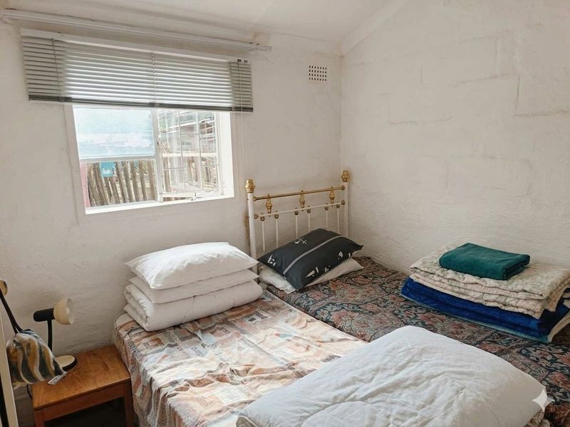 A compact bedroom featuring a window with venetian blinds and textured wall finishes, requiring cosmetic updates to improve the overall aesthetic.