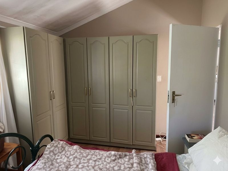 A bedroom featuring built-in cupboards, a sloped ceiling, and laminate flooring.