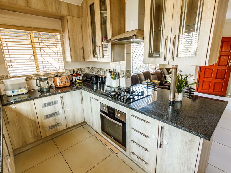 A functional kitchen featuring granite countertops, built-in oven, gas hob, stainless steel extractor fan, and light wood-look cabinetry with ample storage space.