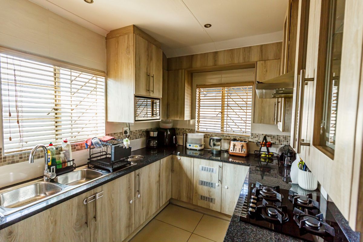 A functional kitchen featuring wood-look laminate cabinetry, granite countertops, a gas hob with extractor fan, and a double basin sink with tiled backsplash.