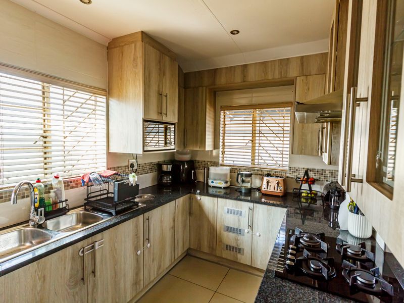 A functional kitchen featuring wood-look laminate cabinetry, granite countertops, a gas hob with extractor fan, and a double basin sink with tiled backsplash.