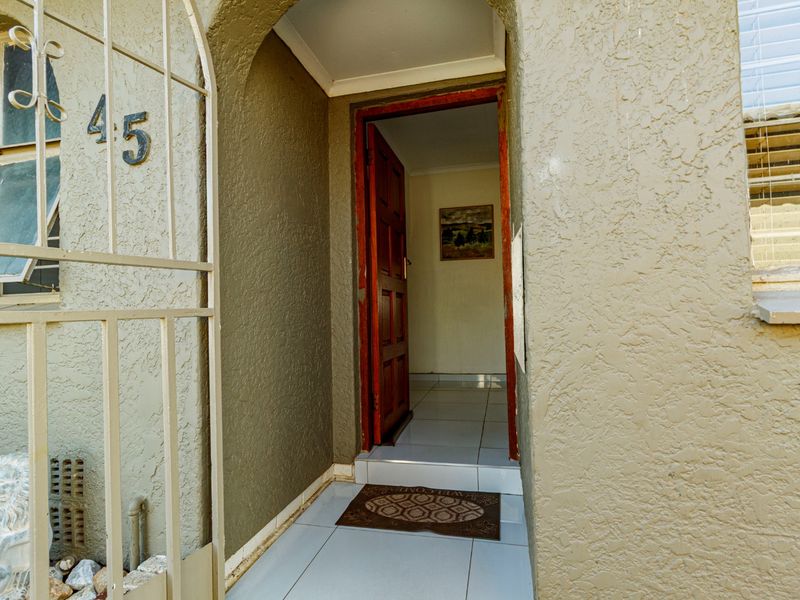 Front entrance featuring a security gate, tiled porch area, and a timber front door leading into the home.
