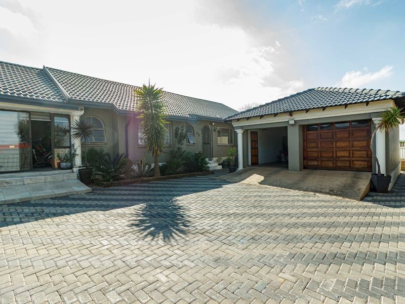 Front elevation of a residential property featuring a paved driveway, double garage with wooden door, and a tiled roof structure.