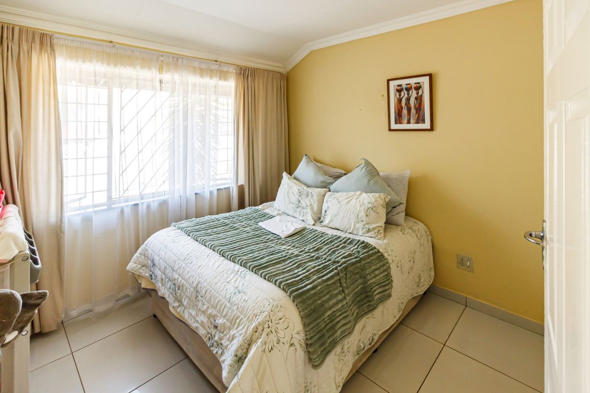 A cozy bedroom featuring tiled flooring, coved ceilings, and a large window fitted with security bars, providing natural light.