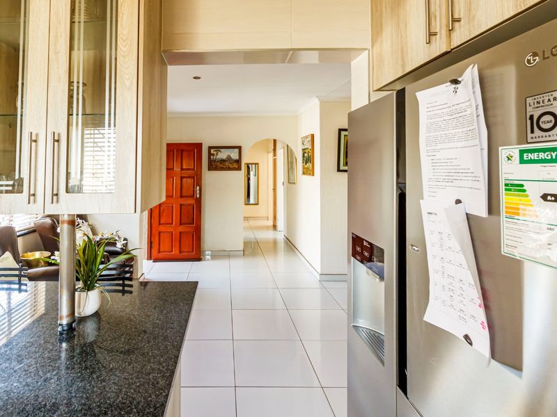 A functional kitchen featuring granite countertops and light wood-look cabinetry, leading into a tiled hallway with an arched entryway.