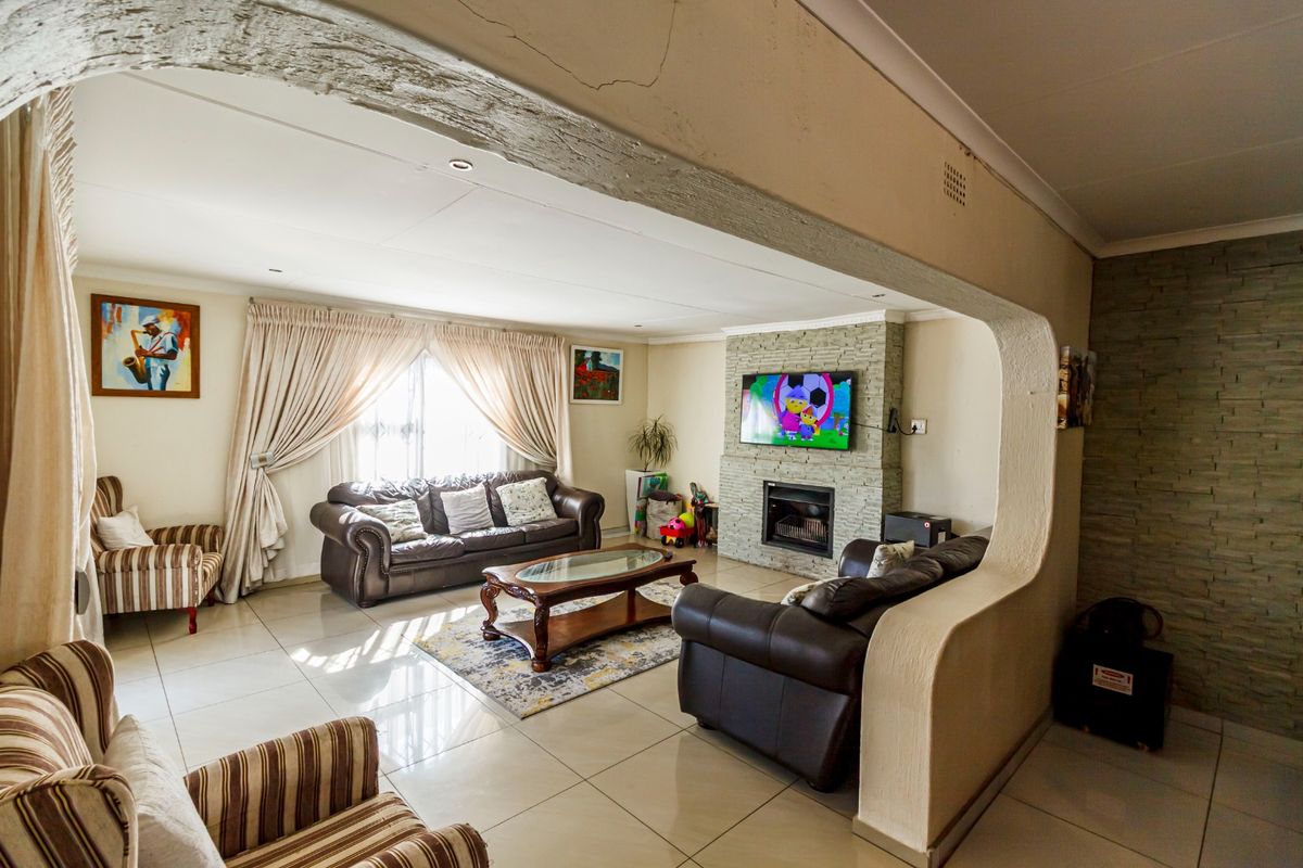Spacious living room featuring a stone-clad fireplace, tiled flooring, and a distinctive architectural archway, offering a comfortable and functional family space.