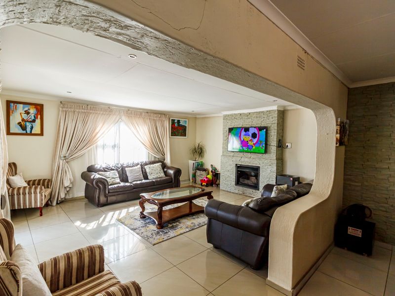 Spacious living room featuring a stone-clad fireplace, tiled flooring, and a distinctive architectural archway, offering a comfortable and functional family space.