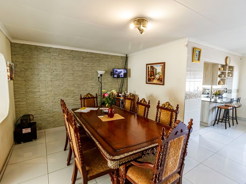 Open-plan dining area featuring a stone accent wall and tiled flooring, seamlessly flowing into a functional kitchen space with a breakfast bar.