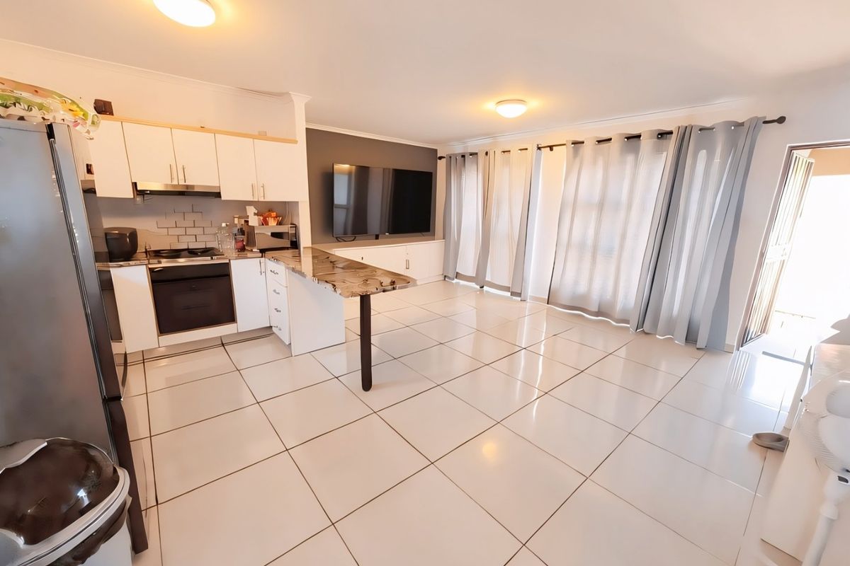 Open-plan living area featuring a modern kitchen with built-in appliances, breakfast counter, and tiled flooring, seamlessly flowing into the lounge space.