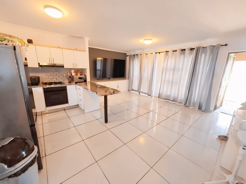 Open-plan living area featuring a modern kitchen with built-in appliances, breakfast counter, and tiled flooring, seamlessly flowing into the lounge space.