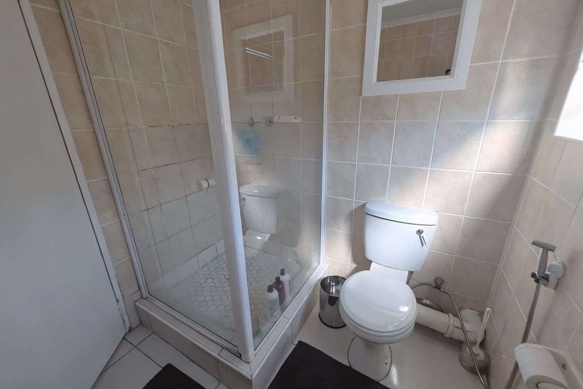 A functional bathroom featuring a glass-enclosed shower, standard toilet, and neutral wall tiling throughout.