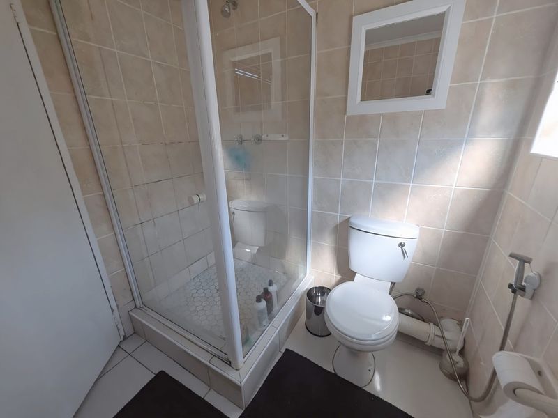 A functional bathroom featuring a glass-enclosed shower, standard toilet, and neutral wall tiling throughout.