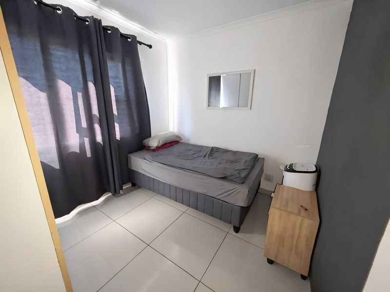 A compact bedroom featuring neutral tiled flooring, white walls, and a dark accent wall, providing a clean and functional living space.