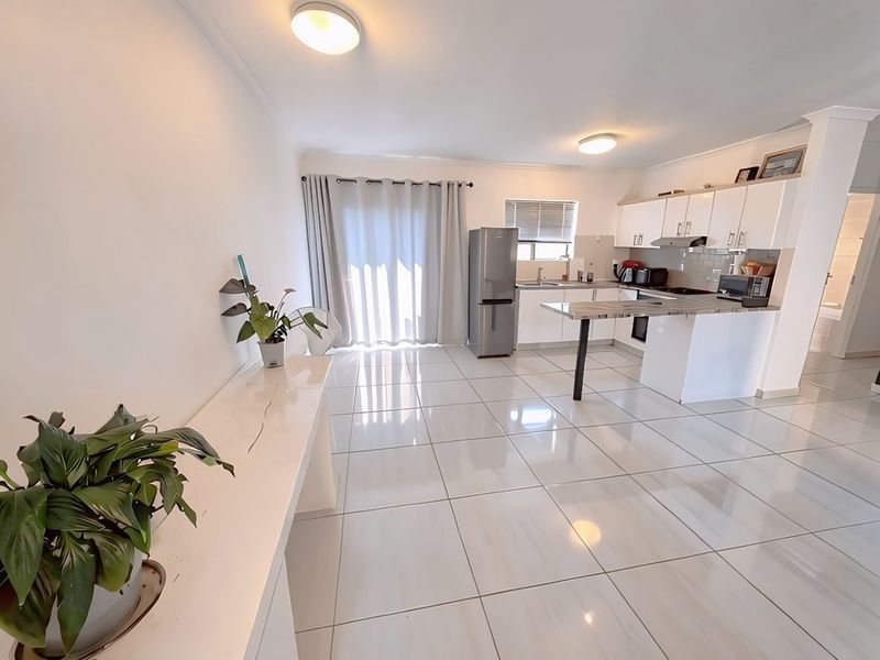 Spacious open-plan living and kitchen area featuring modern white cabinetry, a functional kitchen island, tiled flooring, and direct access to an outdoor space.