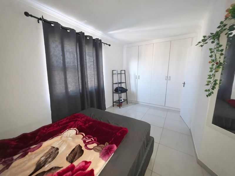 A bedroom featuring white built-in cupboards, tiled flooring, and a window with a curtain rod.