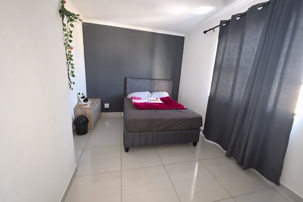A well-lit bedroom featuring neutral tiled flooring, a dark accent wall, and large window with curtain rod installation.