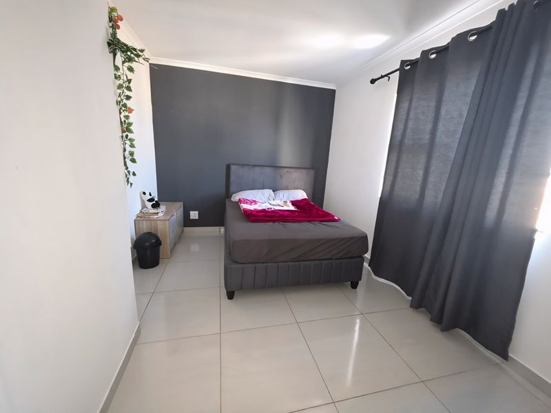 A well-lit bedroom featuring neutral tiled flooring, a dark accent wall, and large window with curtain rod installation.