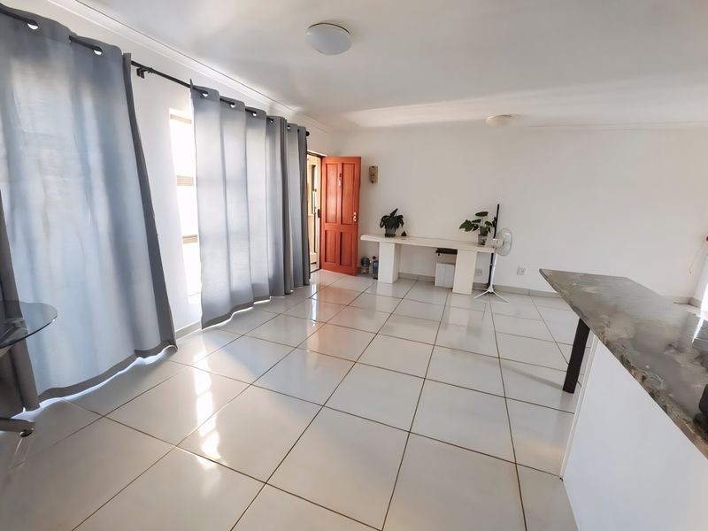 An open-plan living area featuring neutral tiled flooring, a granite breakfast counter, and direct access to the entrance.