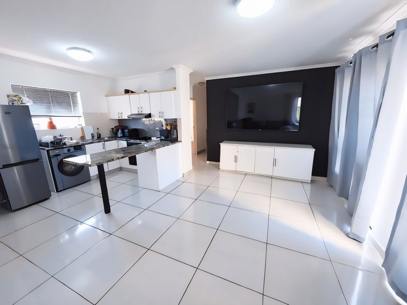 Modern open-plan living area featuring a well-appointed kitchen with stone countertops, sleek white cabinetry, and large format ceramic floor tiles throughout.