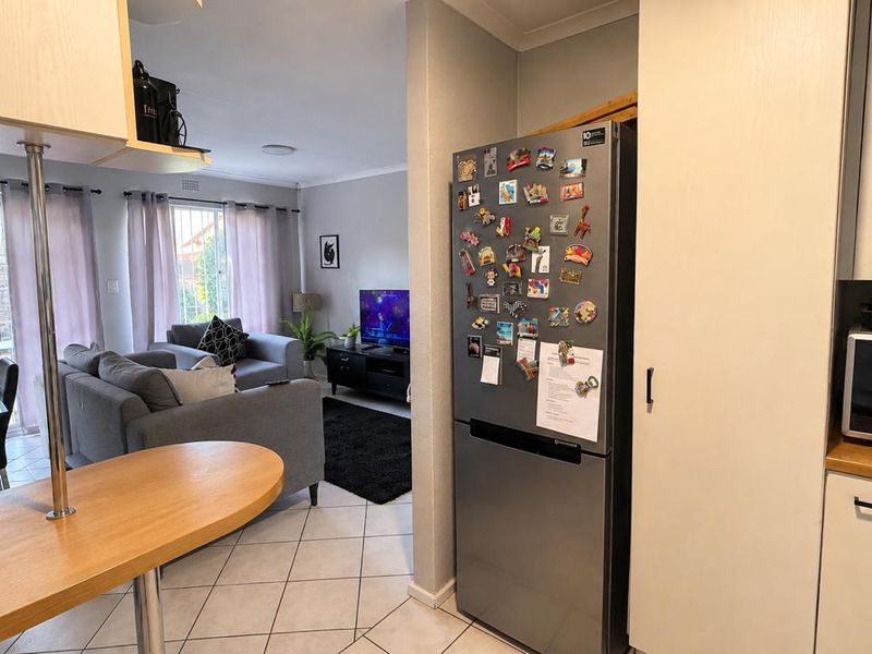 Open-plan living area featuring a kitchen with built-in cabinetry and a breakfast bar, flowing into a comfortable lounge space with tiled flooring.