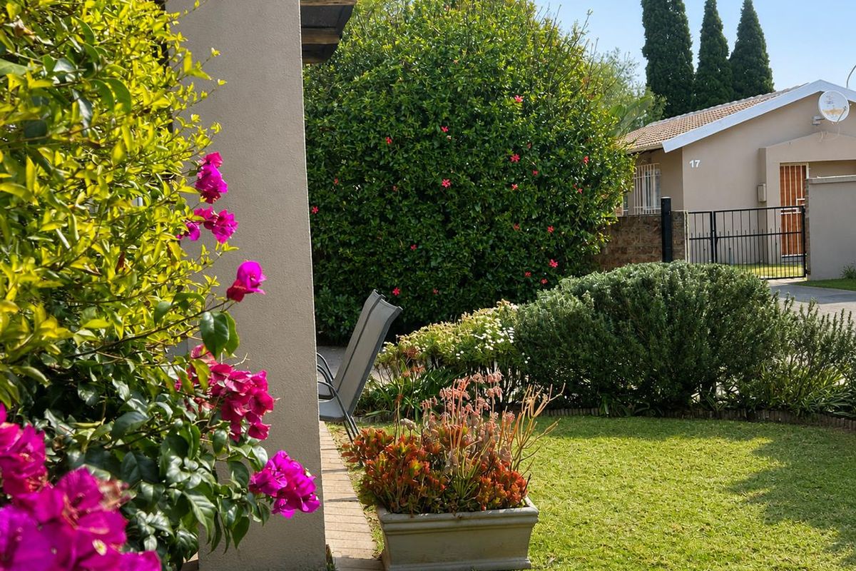A well-maintained private garden area featuring a lush lawn, established shrubbery, and a paved walkway adjacent to the townhouse exterior.