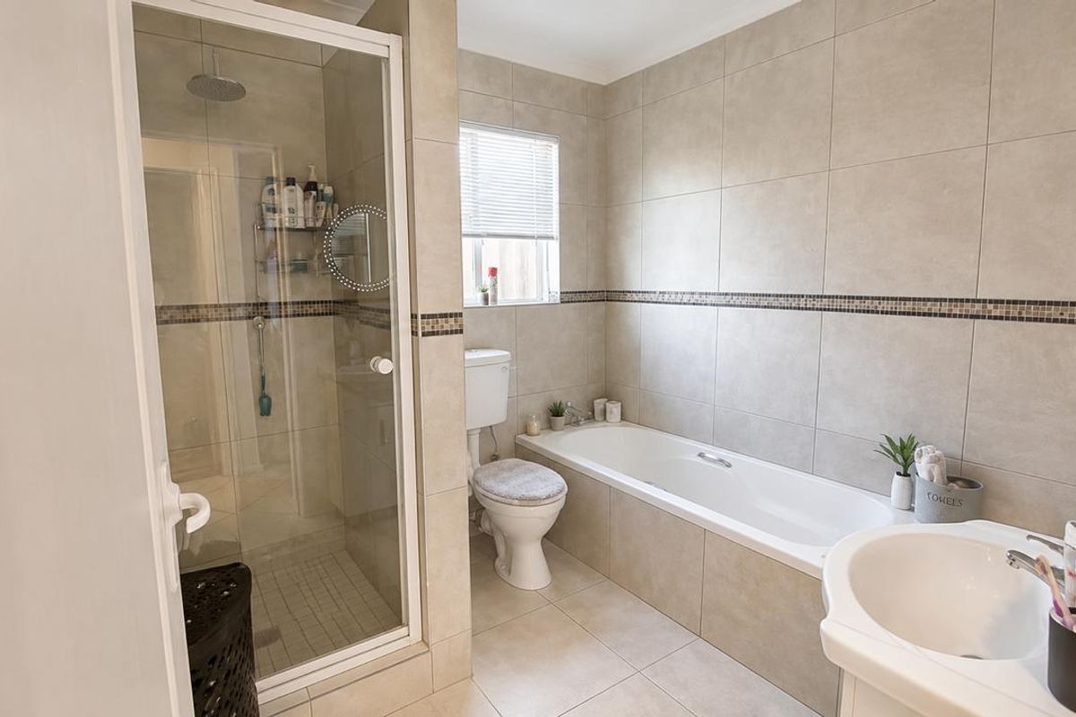 A well-maintained bathroom featuring a glass-enclosed shower, a built-in bathtub, a pedestal basin, and neutral floor-to-ceiling tiling.