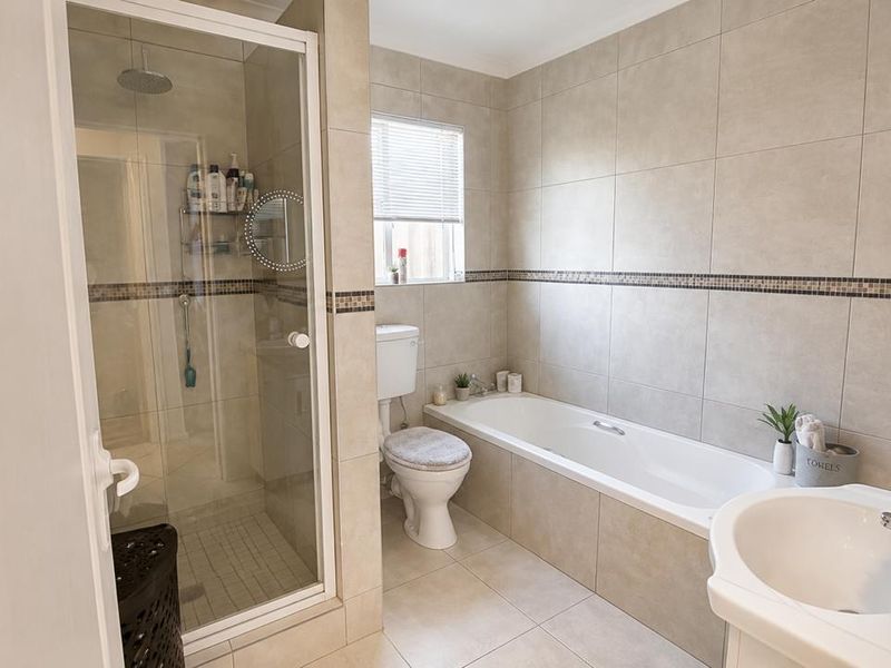 A well-maintained bathroom featuring a glass-enclosed shower, a built-in bathtub, a pedestal basin, and neutral floor-to-ceiling tiling.